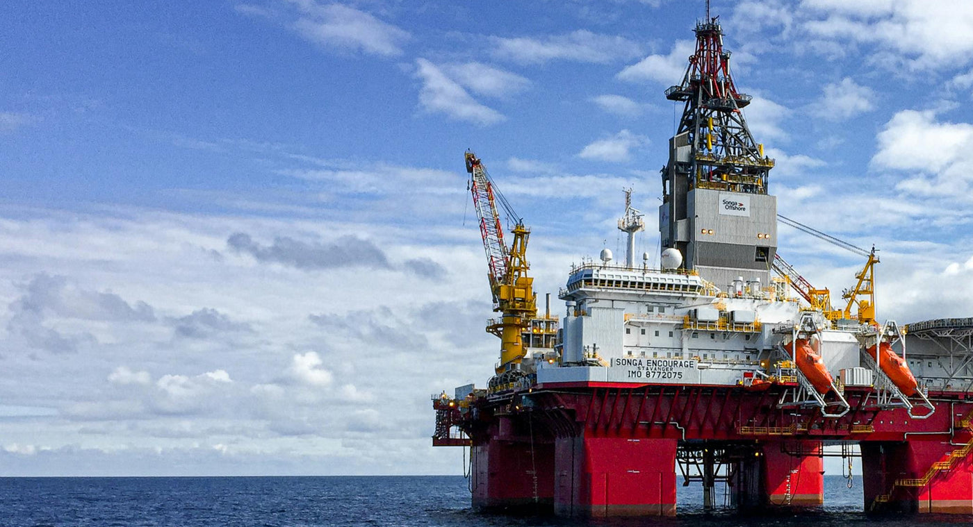 Oil rig in the middle of the ocean with a blue sky and clouds.